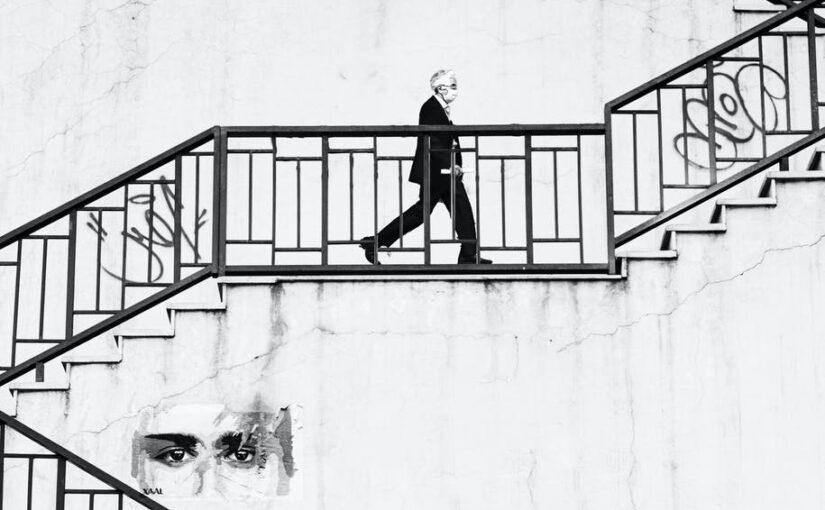 grayscale photo of a man wearing face mask walking up the staircase