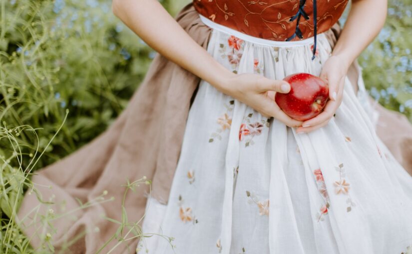 a woman in white and red floral dress holding red apple fruit